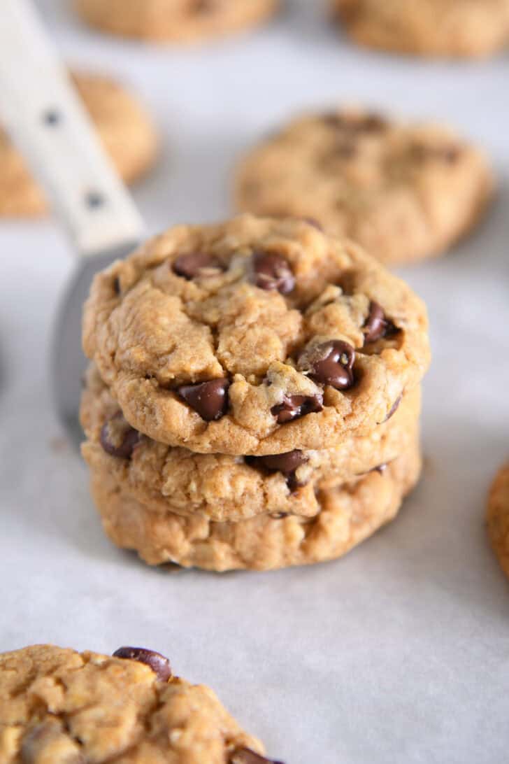 Three pumpkin oatmeal chocolate chip cookies stacked on a spatula.