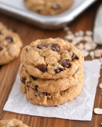 Three brown butter pumpkin oatmeal chocolate chip cookies stacked on square of parchment paper.