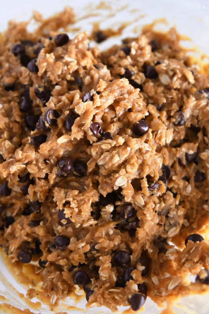 Glass bowl with mixed pumpkin oatmeal chocolate chip cookie batter.