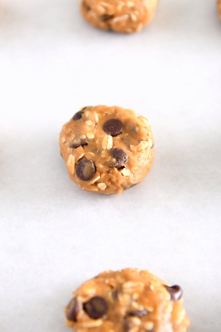 Pumpkin oatmeal chocolate chip cookie dough ball pressed flat on parchment paper.