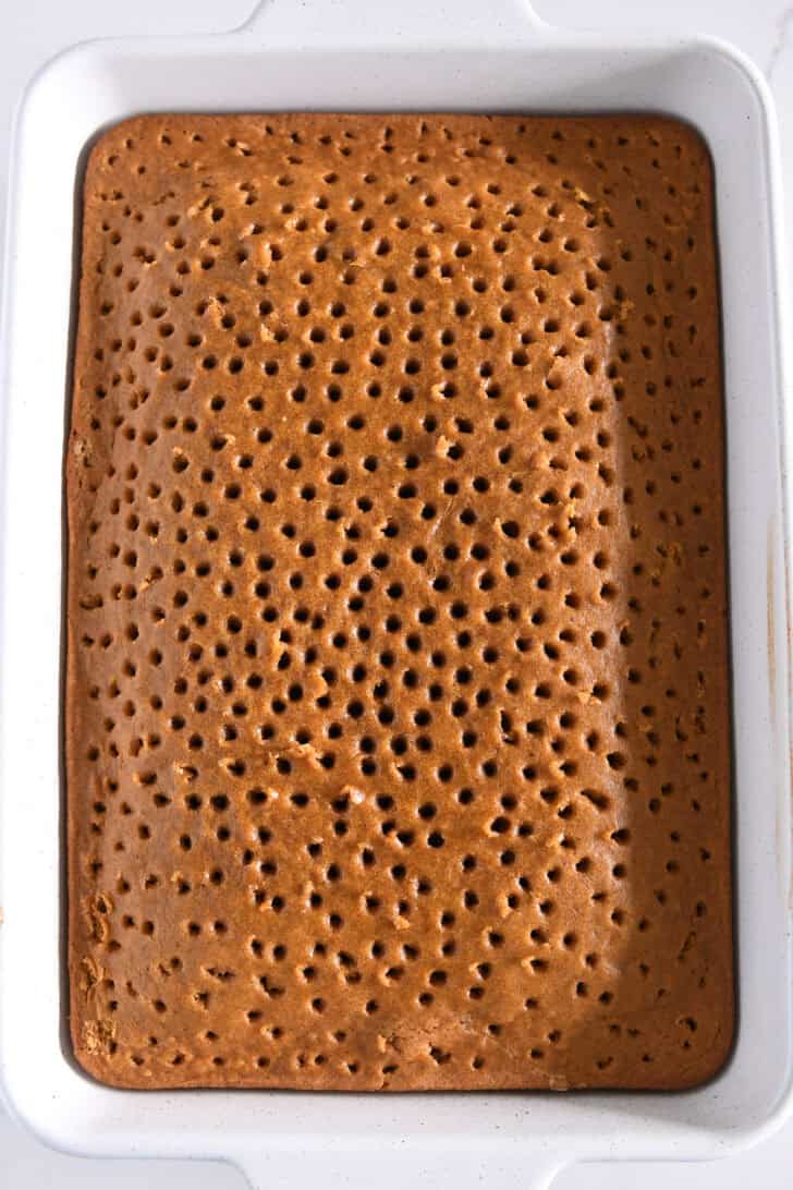 Top down view of pumpkin cake dotted with holes in white 9X13-inch pan.