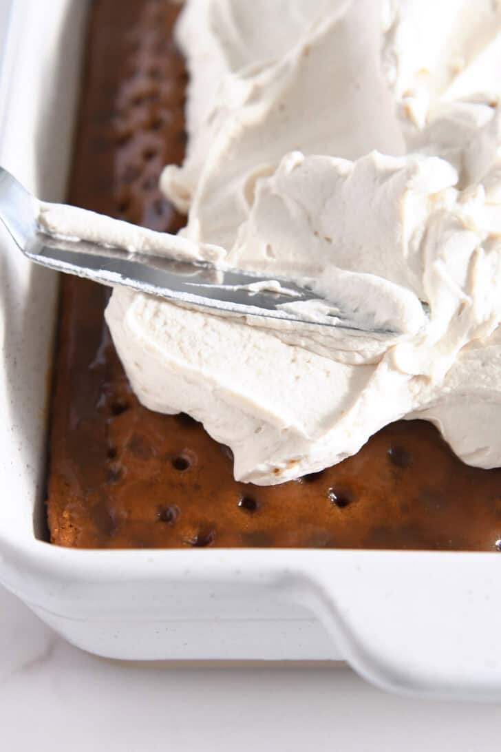 Spreading caramel cream frosting on top of caramel pumpkin poke cake.