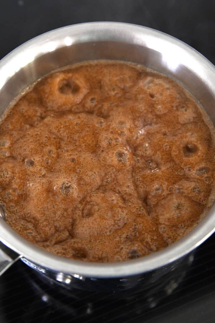 Small pan with bubbling caramel sauce cooking on induction stove.