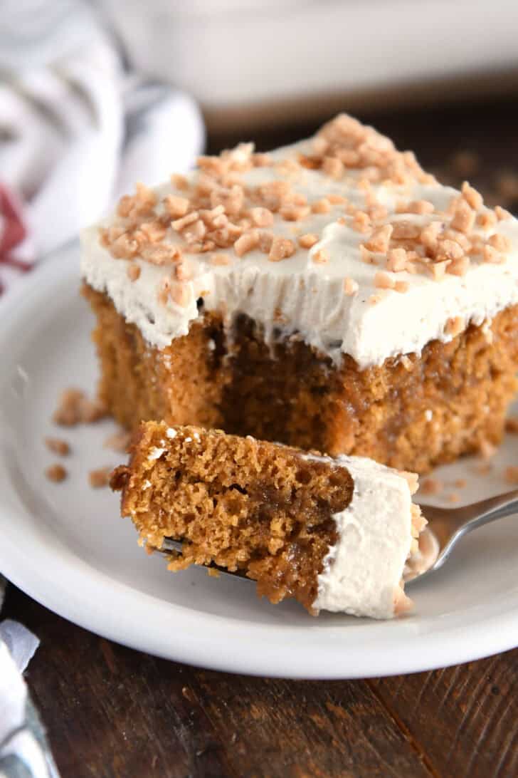 Bite of pumpkin caramel poke cake on fork with square of cake on white plate.