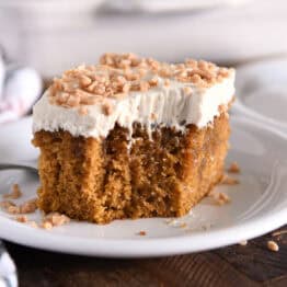 Square of pumpkin caramel poke cake with bite taken out and topped with frosting and toffee bits.