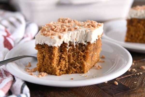 Square of pumpkin caramel poke cake with bite taken out and topped with frosting and toffee bits.
