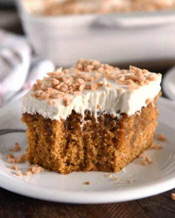 Square of pumpkin caramel poke cake with bite taken out and topped with frosting and toffee bits.