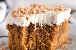 Square of pumpkin caramel poke cake with bite taken out and topped with frosting and toffee bits.