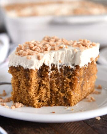 Square of pumpkin caramel poke cake with bite taken out and topped with frosting and toffee bits.