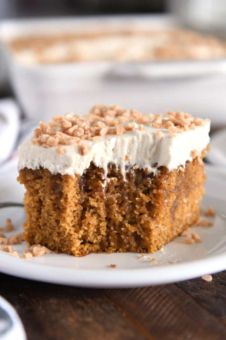 Square of pumpkin caramel poke cake with bite taken out and topped with frosting and toffee bits.