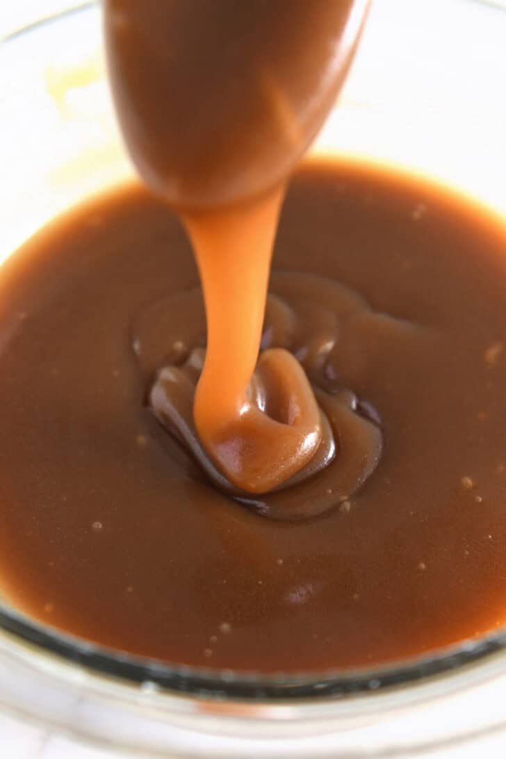 Drizzling thick caramel sauce in glass bowl with spoon.