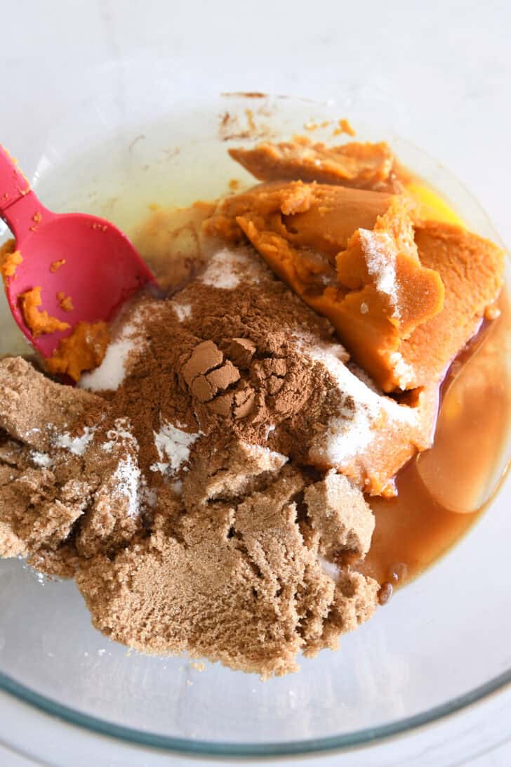 Glass bowl with brown sugar, pumpkin, eggs, oil, cinnamon and salt.