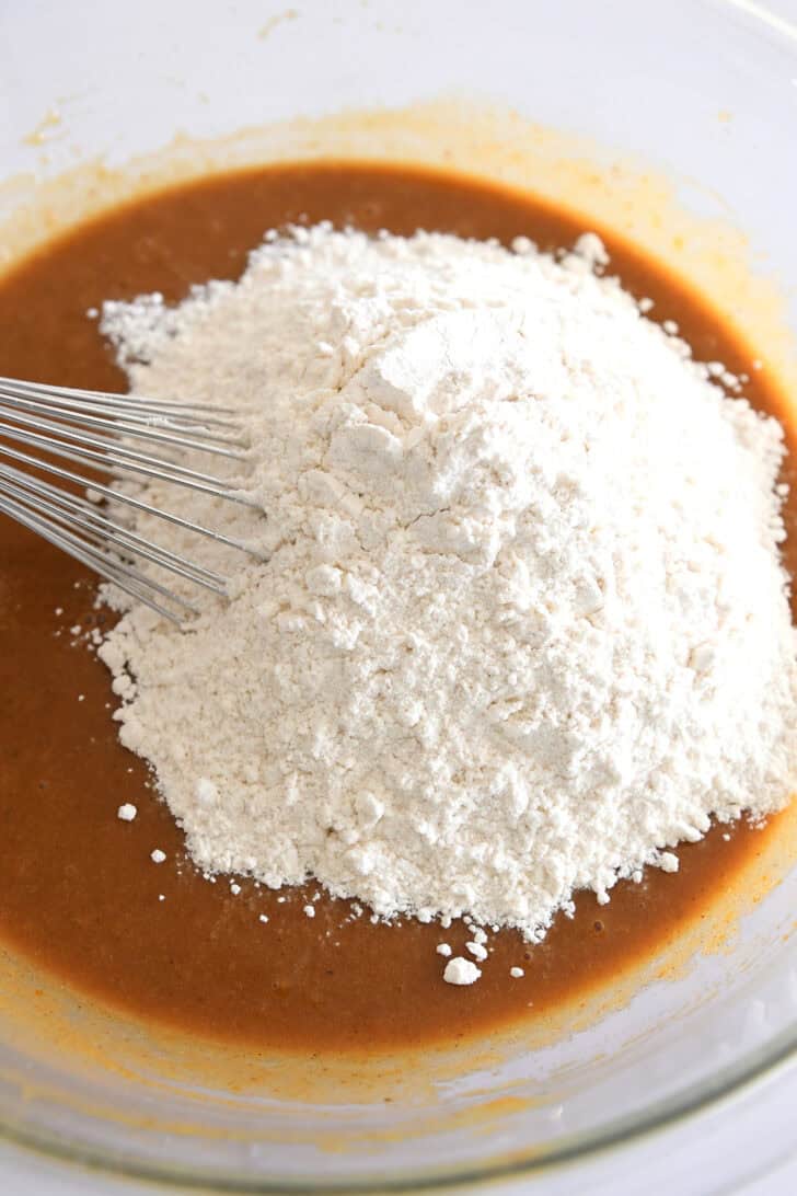Flour in glass bowl with pumpkin cake batter.