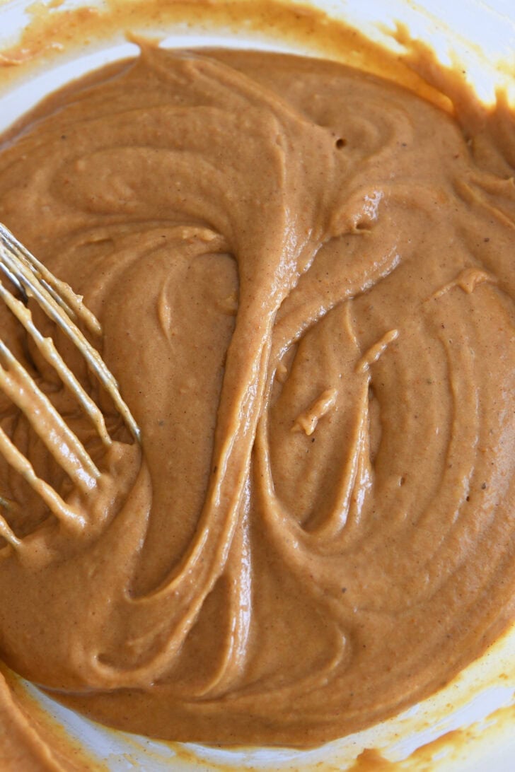 Pumpkin cake batter in glass bowl with whisk.