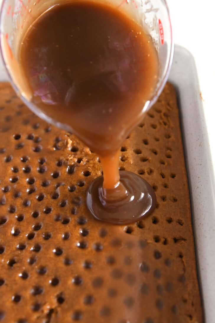 Pouring caramel sauce over the top of a pumpkin cake dotted with holes.