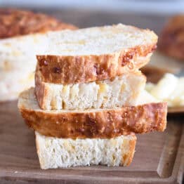 Four half slices of cheesy peasant bread on cutting board with butter.