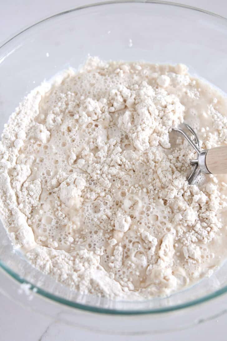 Glass bowl with dry ingredients mixed with water with Danish dough hook.