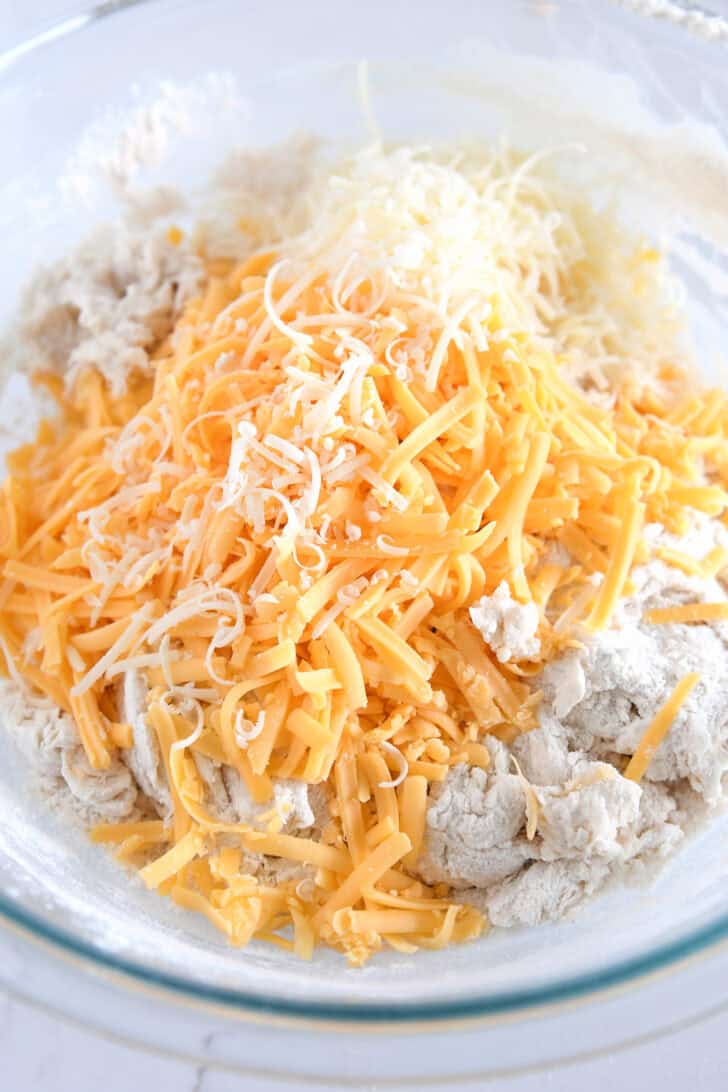 Sharp cheddar cheese and Parmesan cheese on top of bread dough in glass bowl.