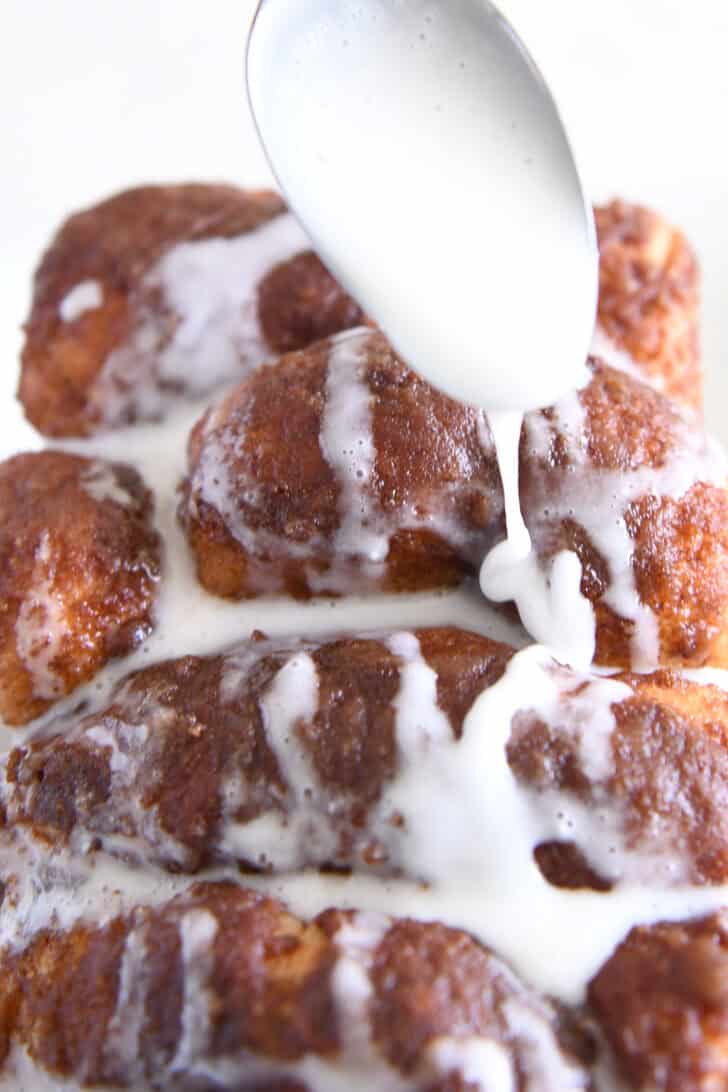 Spoon drizzling glaze over cinnamon bread.