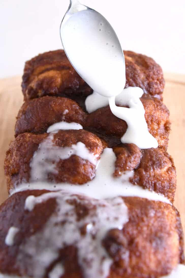 Drizzling powdered sugar glaze with spoon over top of cinnamon bread.