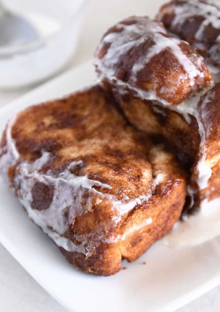Thick slice of glazed cinnamon pull-apart bread with loaf on white platter.
