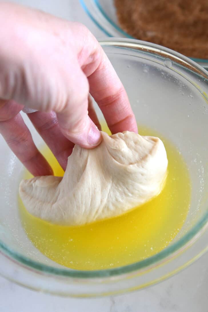 Dipping piece of bread dough in melted butter.