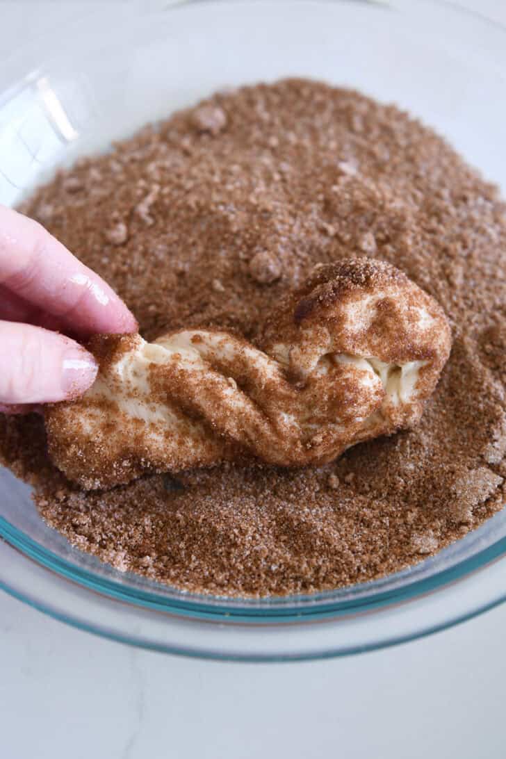 Rolling buttered piece of dough in brown sugar and cinnamon.