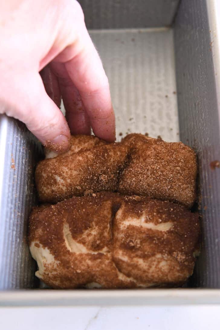 Placing slices of cinnamon and sugar coated dough in loaf pan.