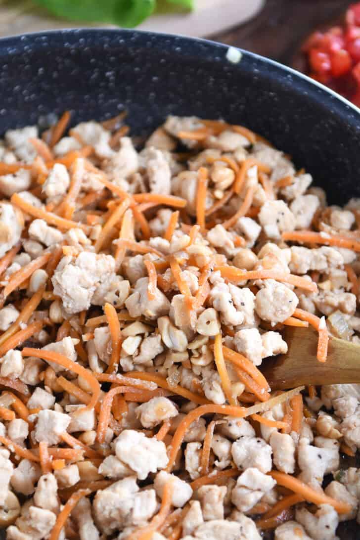 Top down view of a chicken, carrot, and cashew mixture being cooked in a skillet.