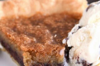 A slice of chocolate chip cookie pie with a bite taken out on a white plate. A scoop of ice cream is next to the pie.