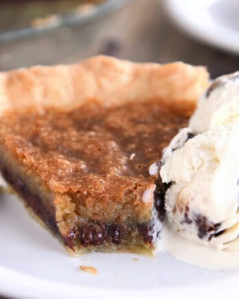 A slice of chocolate chip cookie pie with a bite taken out on a white plate. A scoop of ice cream is next to the pie.