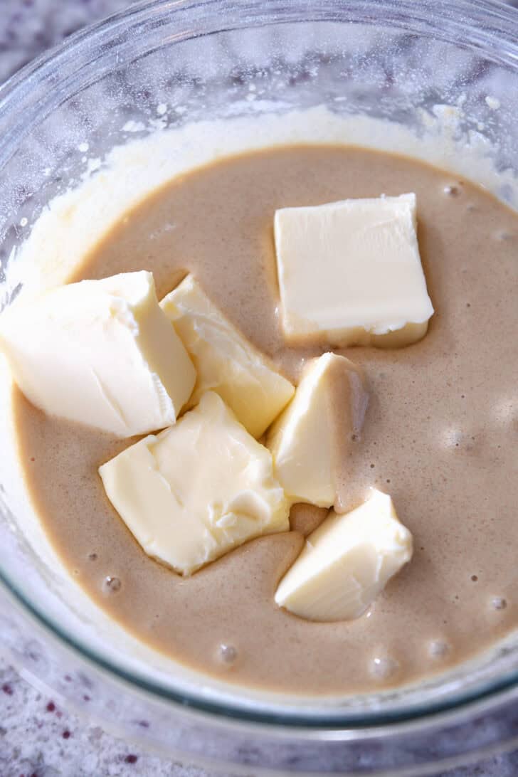 Top down view of batter with a stick of butter cut up in it in a glass bowl.