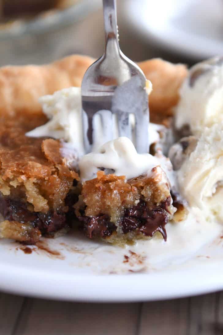 A white plate with a slice of chocolate chip cookie pie and a fork taking a bite out.