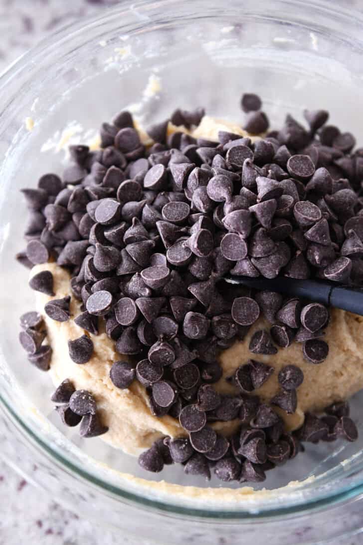 Top down view of chocolate chip cookie dough batter with chocolate chips on top in a glass bowl.