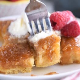 A fork taking a bite out of a caramelized french toast bake on a white plate.
