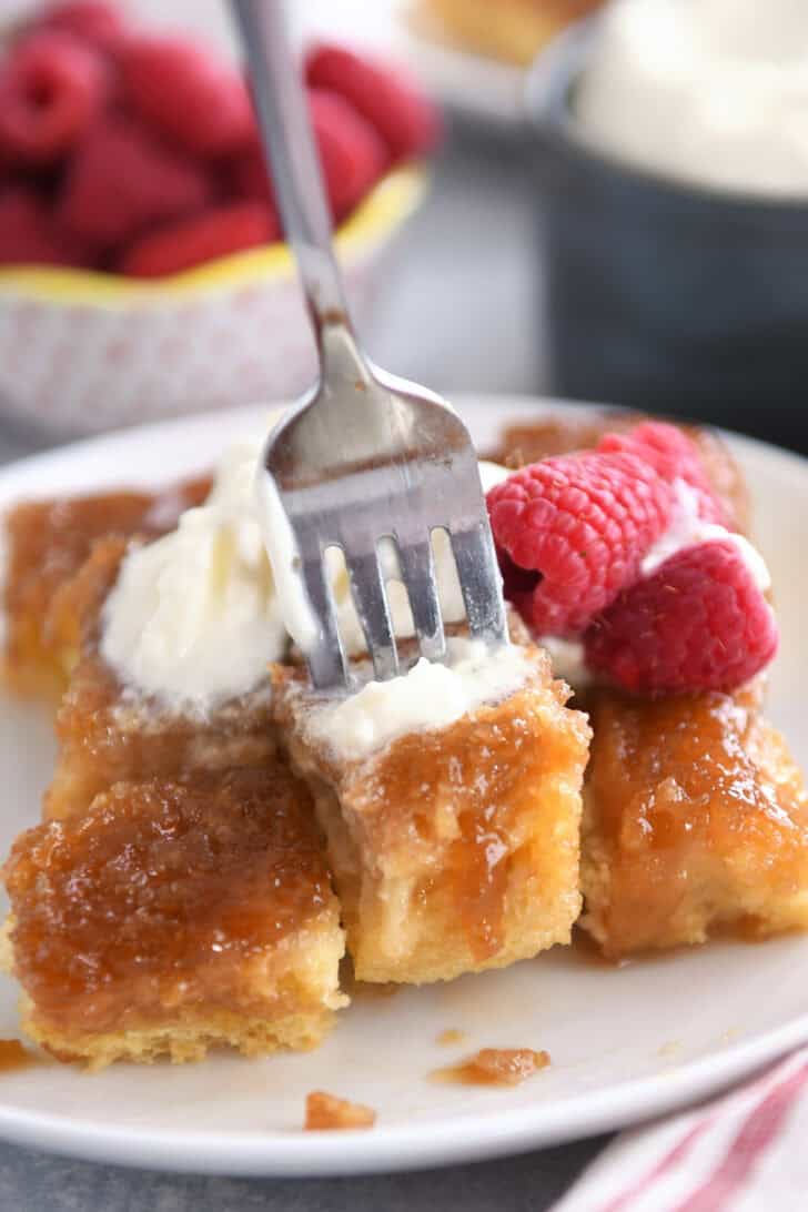 A fork taking a bite out of a caramelized french toast bake on a white plate.