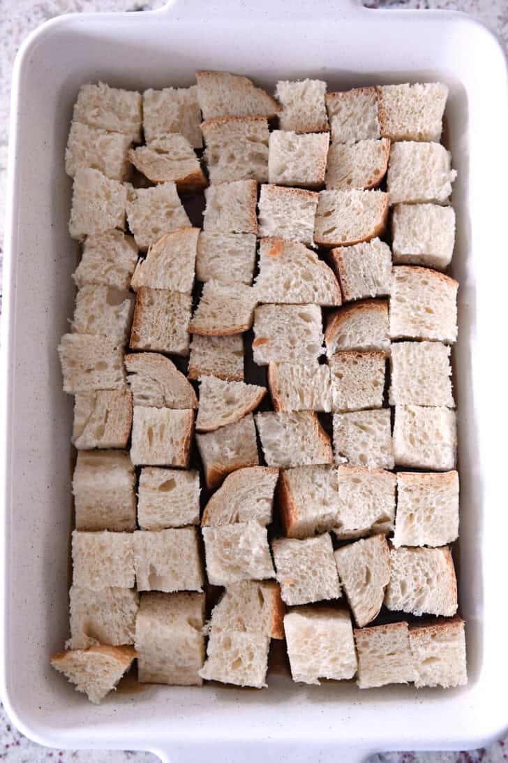Top down view of a white ceramic dish with thick pieces of french bread cut in chunks and layered on the bottom of the dish.