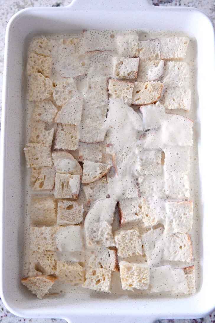 Top down view of a white ceramic dish with a milk mixture covering big chunks of bread.