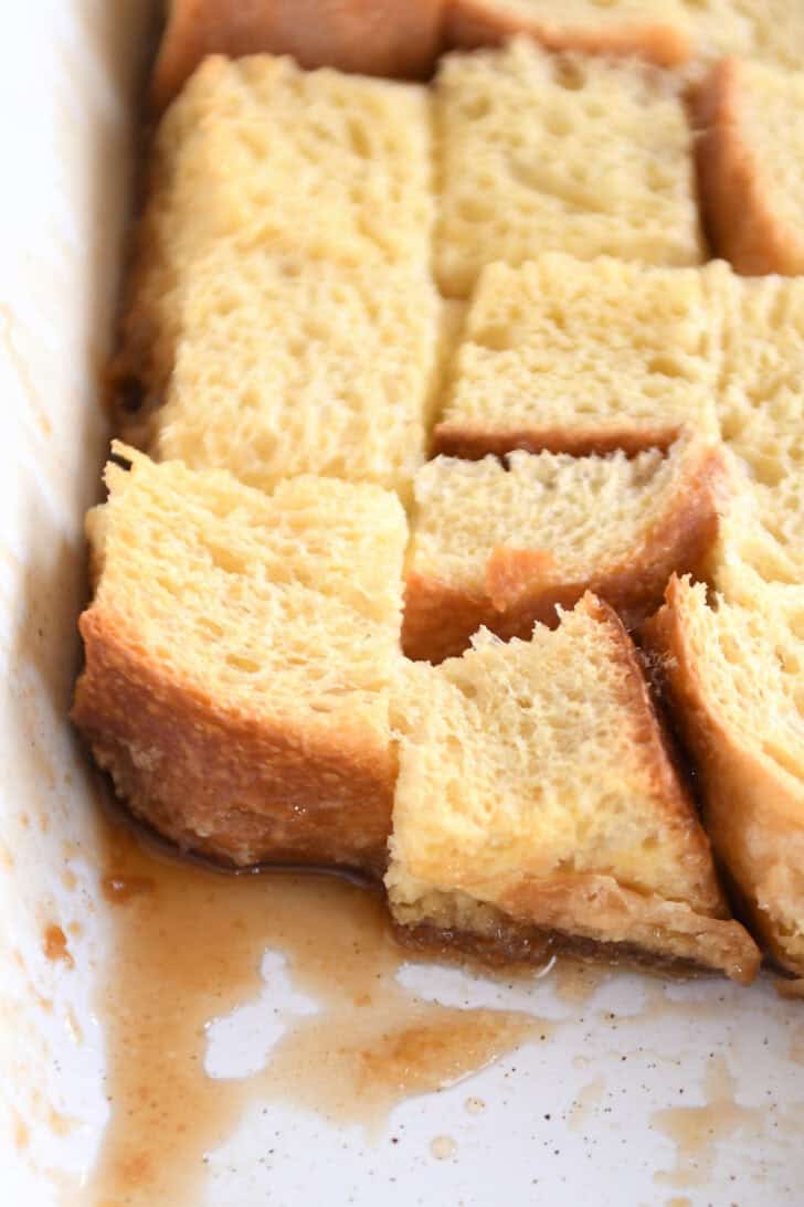 Top down view of a white ceramic dish with egg-coated bread on the bottom of the dish. A portion of the bread is taken out of the corner.
