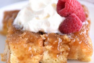 A white plate with a piece of french toast bake topped with whipped cream and fresh raspberries.