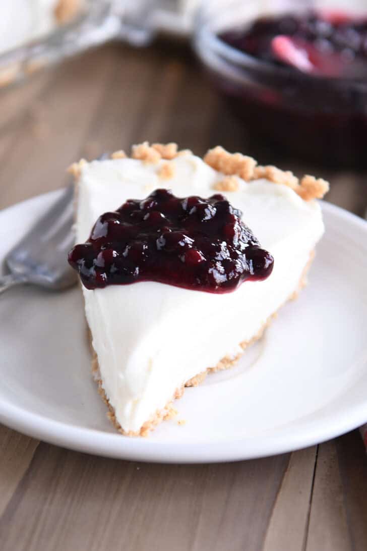 A slice of cheesecake with a dollop of blueberry sauce on top, on a white plate.