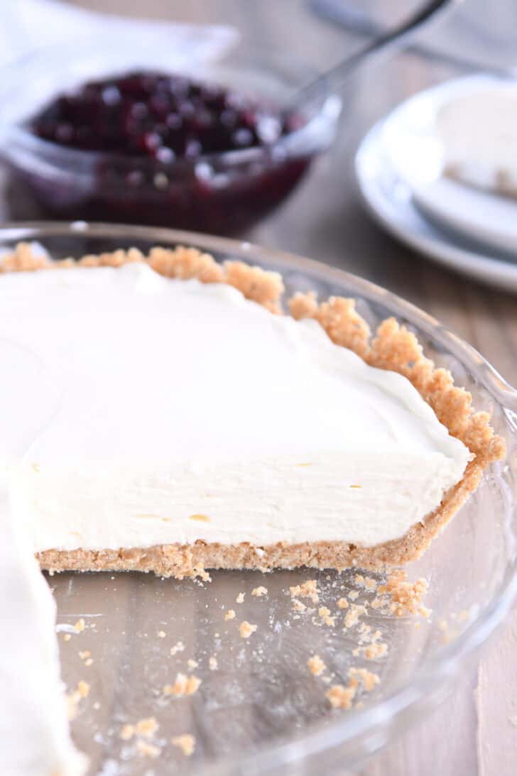 A cheesecake with a graham cracker crust in a glass dish. A large slice is cut out of the cheesecake.