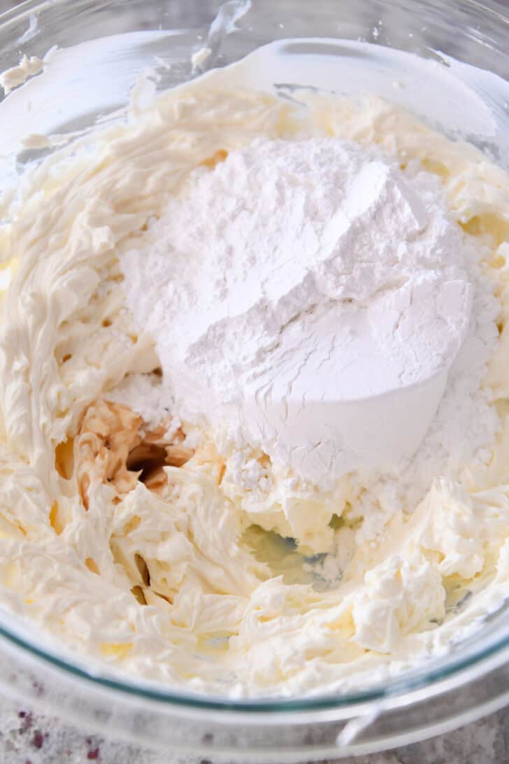 Top down view of whipped cream cheese with flour on top in a glass bowl.