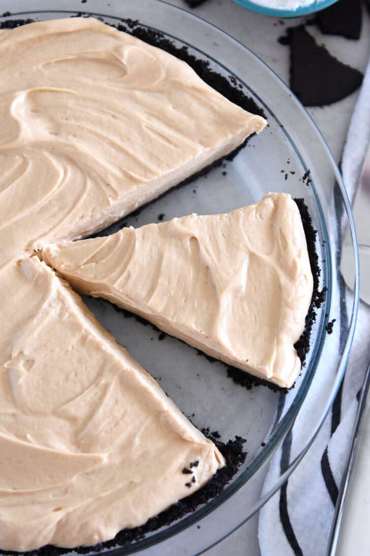 Top down view of a glass pie plate with a creamy peanut butter pie with a few slices cut out.