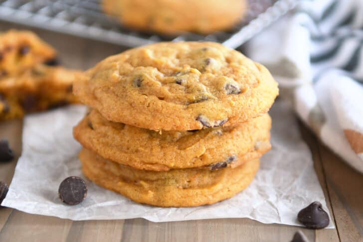 A stack of three pumpkin chocolate chip cookies on a piece of parchment.
