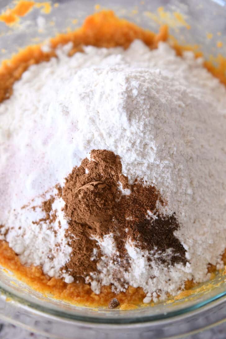 Top down view of flour, spices, and orange pumpkin batter in a glass bowl.
