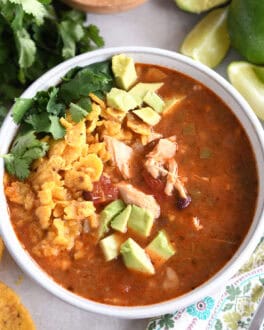 Top down view of a white bowl full of chicken tortilla soup topped with diced avocados, crushed chips, and chopped cilantro.