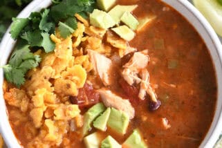 Top down view of a white bowl full of chicken tortilla soup topped with diced avocados, crushed chips, and chopped cilantro.