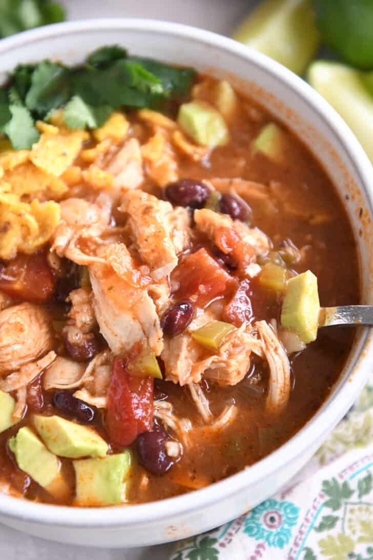 Top down view of a white bowl of chicken tortilla soup topped with diced avocados, crushed chips, and cilantro.