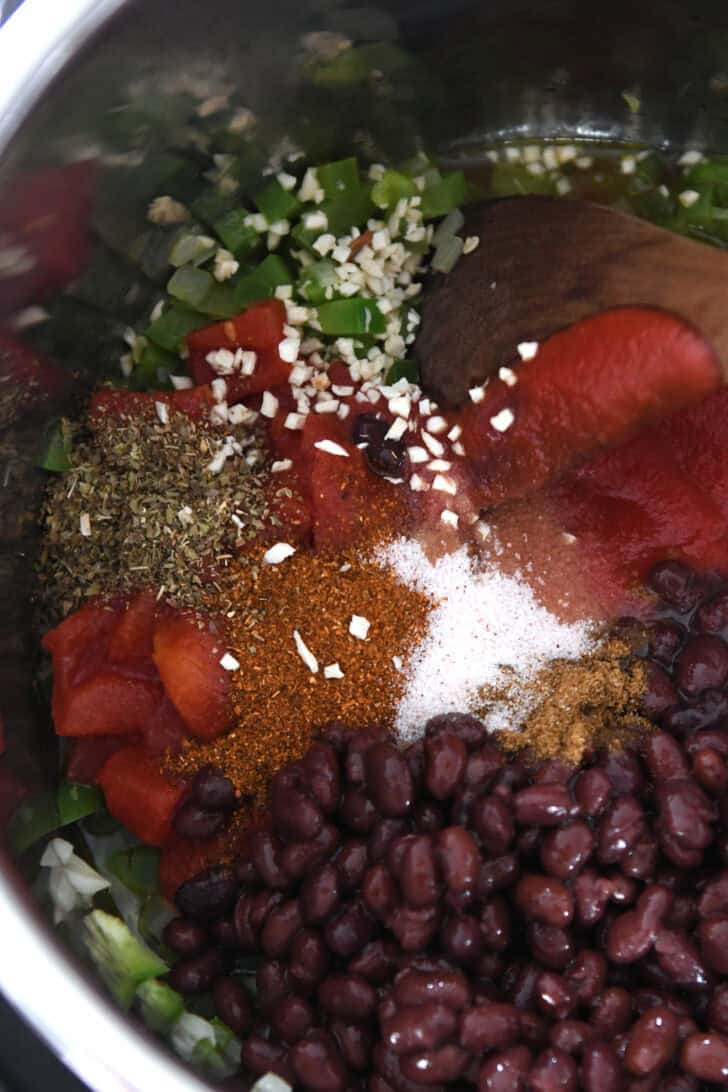 Top down view of an InstantPot filled with black beans, spices, diced green peppers, and crushed tomatoes.